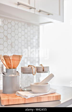 Modernen Küchengeräten unter der Pantry Schränke neben einer Wand mit Wabendesign und mit Sonnenlicht beleuchtet, es gibt Kochlöffel im Krug Stockfoto