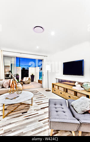 Schickes Wohnzimmer mit Fernseher und Schrank in der Nähe von einem Sofa mit Kissen auf dem Teppich, es ist ein runder Tisch mit phantastischen Elemente neben einer Tür, Co Stockfoto