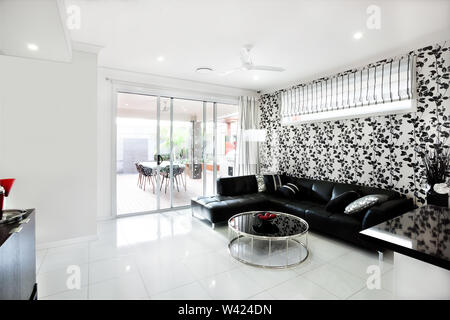 Modernes Wohnzimmer mit einem schwarzen Sofa mit Kissen und eine kreative Runde Tisch wie eine Trommel. Es gibt Früchte in einer Vase. Die Wände sind weiß. Th Stockfoto