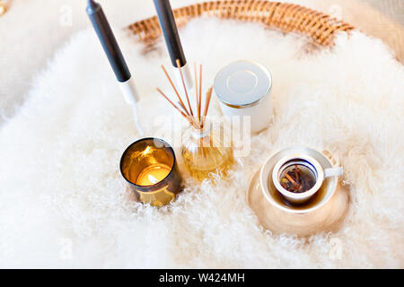 Aroma parfum Flüssigkeit und Stöcke in die Glasflaschen, Keramik Becher auf der Baumwolle oder Wolle Oberfläche mit einer Kerze brennt auf eine Tasse Nahaufnahme Stockfoto