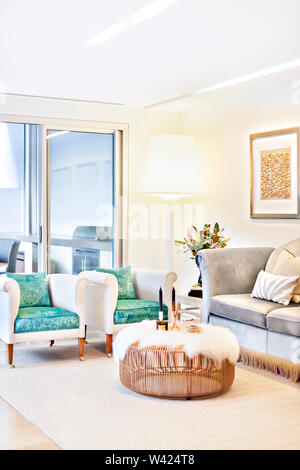 Modernes Wohnzimmer mit Sofas und Tischen einschließlich grüne Kissen, das Glas Fenster aus der hinter und neben dem großen Lampe über der beleuchteten Stockfoto