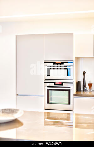 Moderne Küche mit Einbauschränken und Silber Öfen, zu den weißen Wänden, die beleuchtet mit sunlights, der Zähler mit der Fliese su reflektierende ist fixiert Stockfoto
