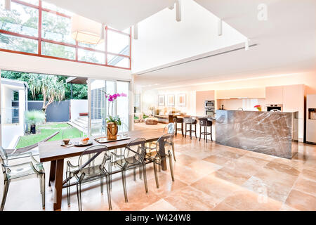 Modernes Haus im Innen- und Außenbereich einschließlich Esszimmer und Küche neben dem Wohnzimmer, der Essbereich oder Terrasse hat einen hölzernen Tisch mit Kunststoff siehe throug Stockfoto