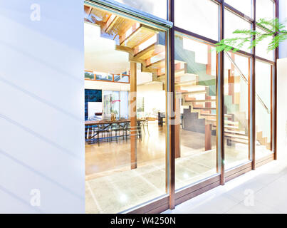 Modernes Haus Glasfenster vom Außenpool mit Holz- Beiträge, die inneren Essbereich und Treppen, die durch die Fenster sehen kann Stockfoto