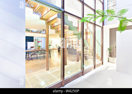 Modernes Haus Glasfenster vom Außenpool mit Holz- Beiträge, die inneren Essbereich und Treppen, die durch die Fenster sehen kann Stockfoto