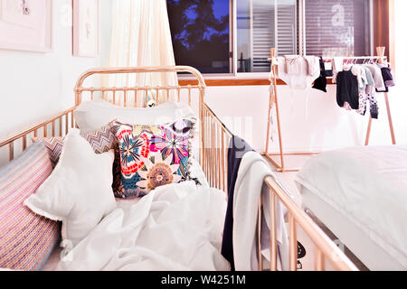 Das kleinere Kind Schlafzimmer mit Kissen und Decken neben der Kleidung auf dem hölzernen Rack in der Nähe der geöffneten Fenster Stockfoto