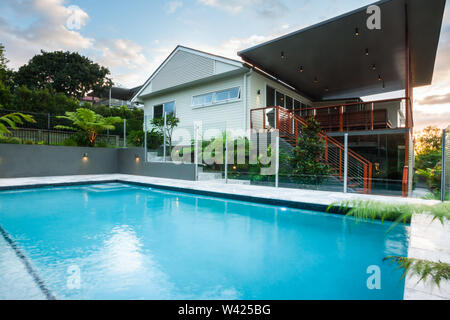 Luxus Pool schließt mit modernen Haus mit grünen Bäumen, unter einem blauen Himmel mit Wolken, gibt es einen hölzernen Treppen und Zaun im Obergeschoss Stockfoto