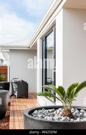 Elegante schwarze hohe Blumentöpfe und Terrasse Stühle vor dem weißen Hintergrund des Hauses und Holzböden. Stockfoto