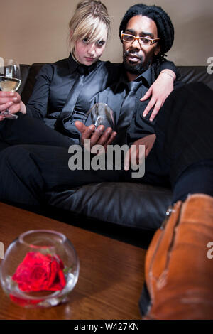 Frau und Mann Wein trinken und Sitzen auf einem Sofa, luxuriöse Haus oder Hotel im Zimmer, tagsüber Szene mit perfekter Beleuchtung, Sie genießen ein Festival o Stockfoto