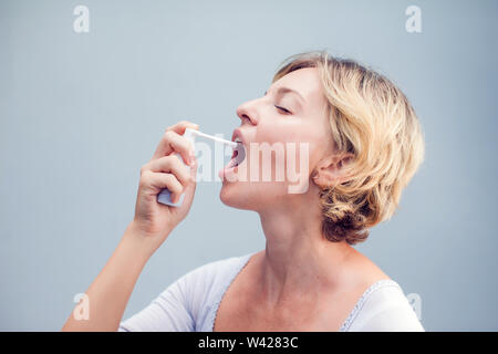 Spray für Halsschmerzen. Foto einer Frau, die ihren Hals behandelt mit einem Spray und streut es in ihrem Mund. Das Konzept von Gesundheit und Krankheit. Stockfoto