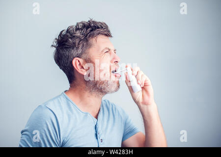 Spray für Halsschmerzen. Foto von einem Mann, der seine Kehle behandelt mit einem Spray und streut es in den Mund. Das Konzept von Gesundheit und Krankheit. Stockfoto