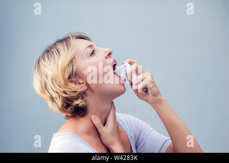 Spray für Halsschmerzen. Foto einer Frau, die ihren Hals behandelt mit einem Spray und streut es in ihrem Mund. Das Konzept von Gesundheit und Krankheit. Stockfoto