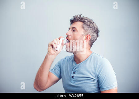 Spray für Halsschmerzen. Foto von einem Mann, der seine Kehle behandelt mit einem Spray und streut es in den Mund. Das Konzept von Gesundheit und Krankheit. Stockfoto