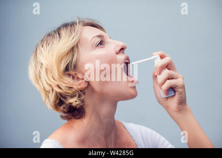 Spray für Halsschmerzen. Foto einer Frau, die ihren Hals behandelt mit einem Spray und streut es in ihrem Mund. Das Konzept von Gesundheit und Krankheit. Stockfoto