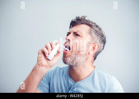 Spray für Halsschmerzen. Foto von einem Mann, der seine Kehle behandelt mit einem Spray und streut es in den Mund. Das Konzept von Gesundheit und Krankheit. Stockfoto