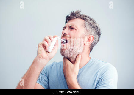 Spray für Halsschmerzen. Foto von einem Mann, der seine Kehle behandelt mit einem Spray und streut es in den Mund. Das Konzept von Gesundheit und Krankheit. Stockfoto