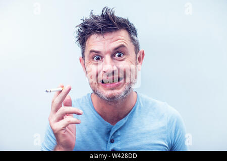 Hübscher junger Mann mit dem braunen Haar tragen Shirt auf grauem Hintergrund. Rauchen Zigarette. balack Zahn Stockfoto