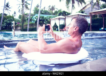 Junger Mann relaxen am Pool, mit Handy. Arbeit und Entspannung Stockfoto