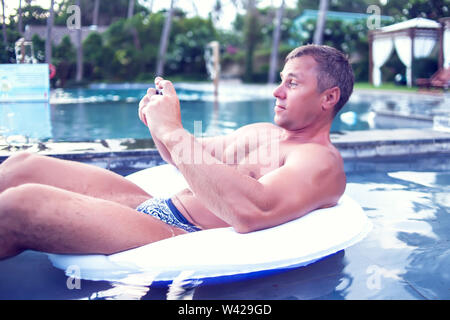 Junger Mann relaxen am Pool, mit Handy. Arbeit und Entspannung Stockfoto