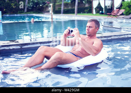 Junger Mann relaxen am Pool, mit Handy. Arbeit und Entspannung Stockfoto
