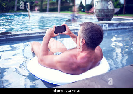 Junger Mann relaxen am Pool, mit Handy. Arbeit und Entspannung Stockfoto
