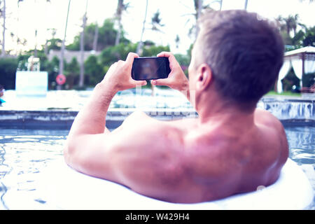 Junger Mann relaxen am Pool, mit Handy. Arbeit und Entspannung Stockfoto