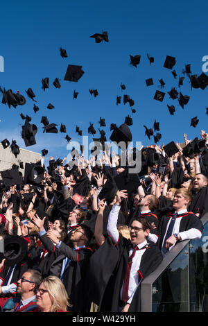 Höhere Bildung in Großbritannien - erfolgreiche Studenten an der Abschlussfeier in Aberystwyth University, nach ihrem Grad erhalten, werfen ihre Mörser board Kappen in der Luft in der Feier. Juli 2019 Stockfoto