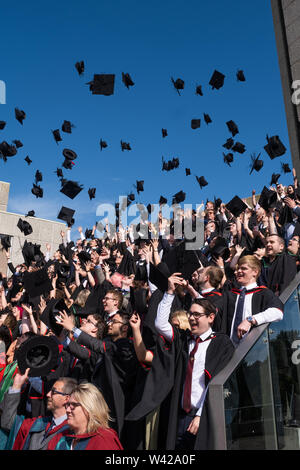 Höhere Bildung in Großbritannien - erfolgreiche Studenten an der Abschlussfeier in Aberystwyth University, nach ihrem Grad erhalten, werfen ihre Mörser board Kappen in der Luft in der Feier. Juli 2019 Stockfoto