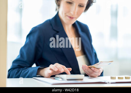 Geschäftsfrau Arbeiten am Rechner mit Goldmünzen auf ihre weißen Schreibtisch. Fokus auf ihre Hand und Euro-banknoten. Stockfoto