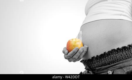Nahaufnahme der Hand einer jungen schwangeren Frau mit einem reifen Apfel gegen Ihren geschwollenen Bauch und Baby bump in einem Konzept der gesunden Ernährung und Diät du Stockfoto