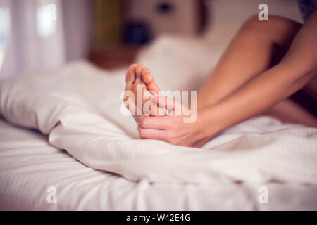 Fußschmerz Frau sitzt auf dem Bett ihre Füße in schmerzende Füße und Stretching Muskeln holding Müdigkeit Schmerzen zu lindern. Menschen und Gesundheit Konzept. Stockfoto