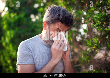 Mann blasen Nase vor der blühenden Baum. Frühling Allergie und Gesundheit Konzept Stockfoto
