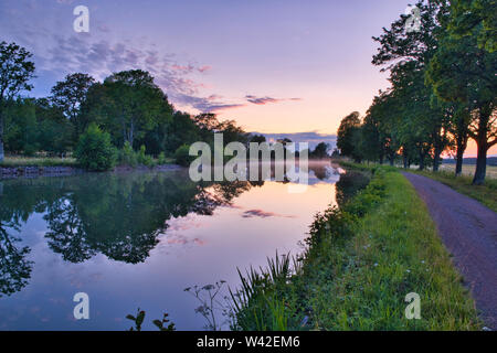 Nebel auf einem Kanal mit Bäumen entlang der Seiten und den Sonnenuntergang im Hintergrund Stockfoto