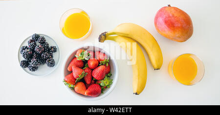 Frisches Obst und Orangensaft isoliert auf Weiss. Gesundes Frühstück für zwei. Banane, Erdbeere, Blackberry und Mango. Ansicht von oben Stockfoto