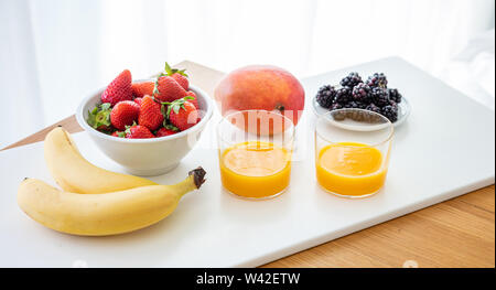 Frisches Obst und Orangensaft isoliert auf Weiss. Gesundes Frühstück für zwei. Banane, Erdbeere, Blackberry und Mango. Nähe zu sehen. Stockfoto