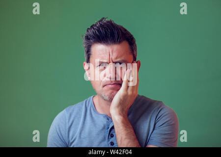 Portrait von frowing junger Mann in Freizeitkleidung holding Palm auf seiner Wange. Menschen, Emotionen und Lifestyle Konzept. Stockfoto