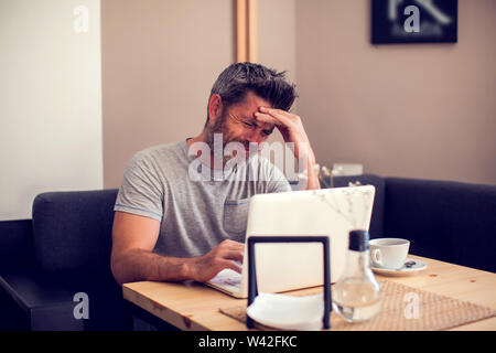 Mann mit einem Kopfschmerzen vor dem Laptop. Menschen, Gesundheit und Technologie Konzept Stockfoto