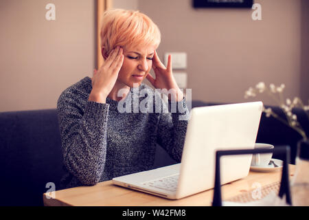 Betonte Frau arbeiten mit Laptop Gefühl Kopfschmerzen. Menschen, Gesundheit und Technologie Konzept Stockfoto