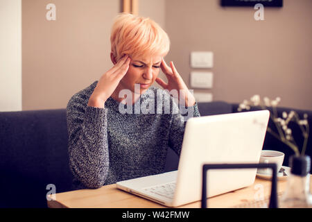 Betonte Frau arbeiten mit Laptop Gefühl Kopfschmerzen. Menschen, Gesundheit und Technologie Konzept Stockfoto