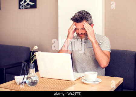 Mann mit einem Kopfschmerzen vor dem Laptop. Menschen, Gesundheit und Technologie Konzept Stockfoto