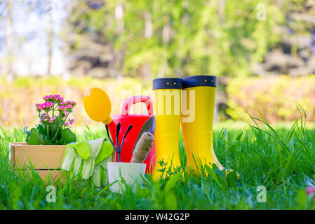 Gummistiefel neben der Tools für die Arbeit im Garten sind auf einem grünen Rasen im Frühjahr Stockfoto