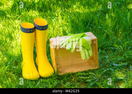 Holz-, grüner Handschuhe und gelbe Gummistiefel auf üppigen Gras im Hinterhof des Hauses Stockfoto