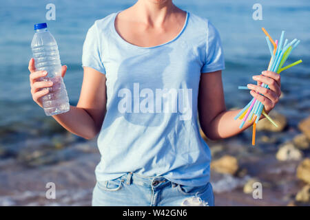 Frau hält Plastikflasche und Strohhalme in die Hände an den Strand. Kunststoff Verschmutzung Konzept. Stockfoto