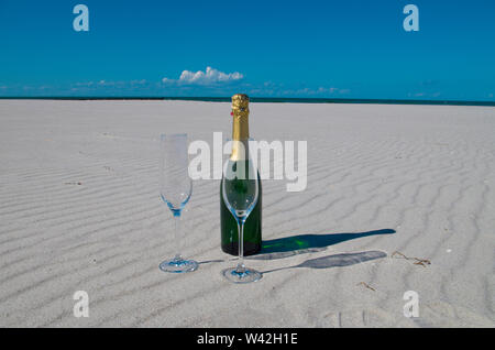 Eine Flasche Champagner am Strand gebaut, weißem Sand und blauem Meer ist ein Urlaub im Paradies. Stockfoto