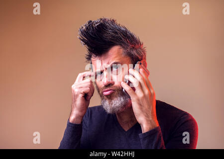 Bärtiger Mann denken und die Suche nach einem auf seine smart phone Chat. Menschen, Emotionen und Technik Konzept Stockfoto