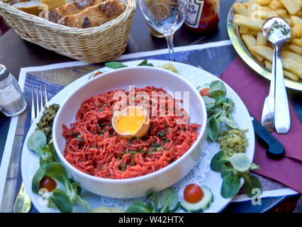 Steak-Tatar ist ein Fleischgericht aus gemahlenem oder Hackfleisch, das mit Zwiebeln, Kapern, Worchestiersauce und anderen serviert wird und mit einem rohen Ei bestockt ist. Stockfoto