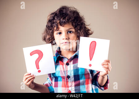 Denken kid Boy hält Frage- und Ausrufezeichen Zeichen Stockfoto