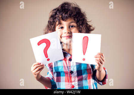 Denken kid Boy hält Frage- und Ausrufezeichen Zeichen Stockfoto