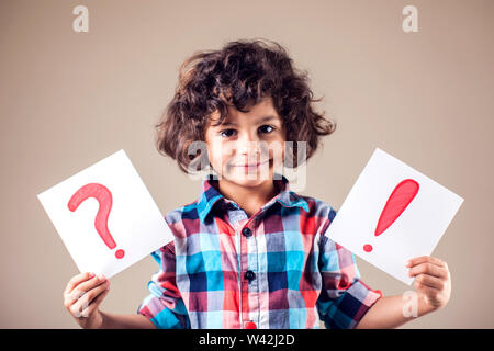 Denken kid Boy hält Frage- und Ausrufezeichen Zeichen Stockfoto