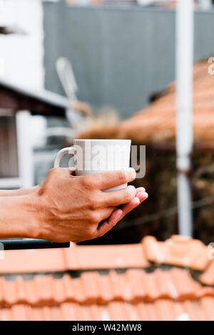 Nahaufnahme eines jungen kaukasischen Mann einen Kaffee auf dem Balkon seiner Wohnung, Hotel oder Ferienwohnung in der Altstadt von einer europäischen Stadt Stockfoto